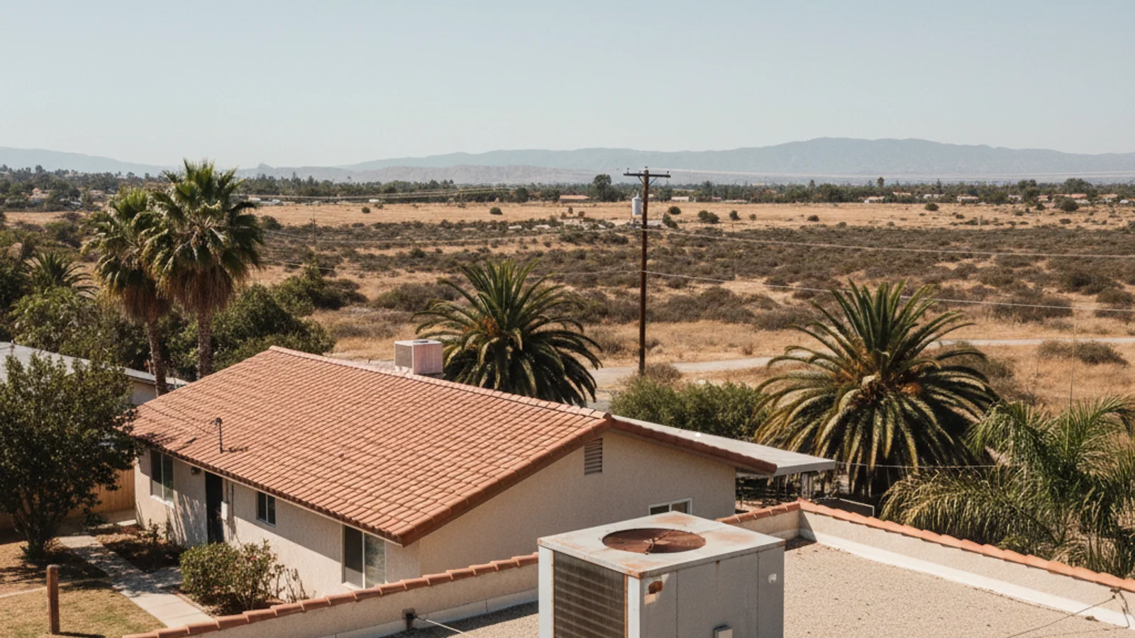 A rooftop evaporative swamp cooler mounted on an older single-story East County San Diego home with dry hills behind it